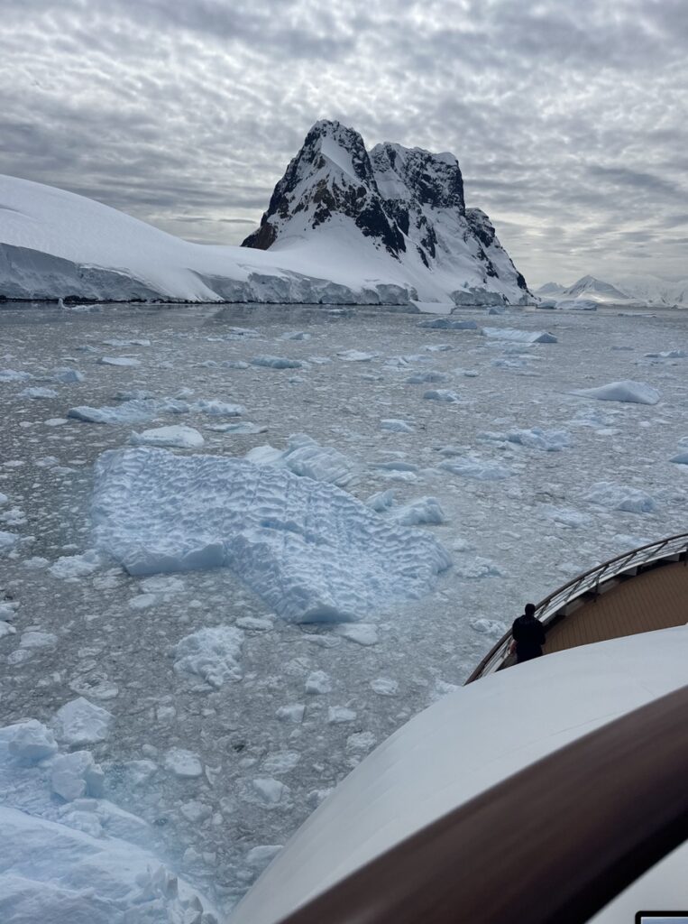 View from a boat of a snow-covered Antarctic peak surrounded by floating sea ice