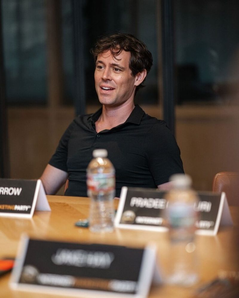 John Arrow smiling during a panel discussion at a conference table